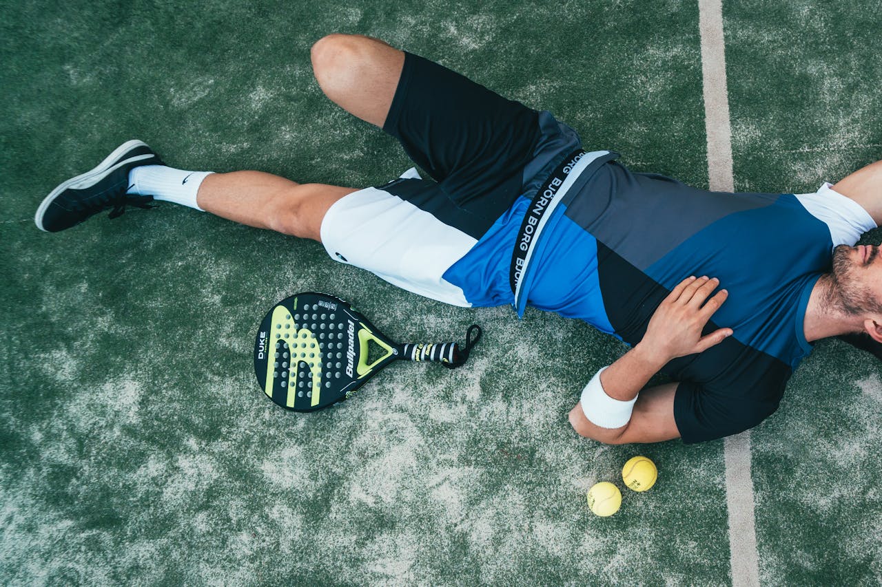 heros-img Tired young athlete resting on padel court with racket and balls nearby.